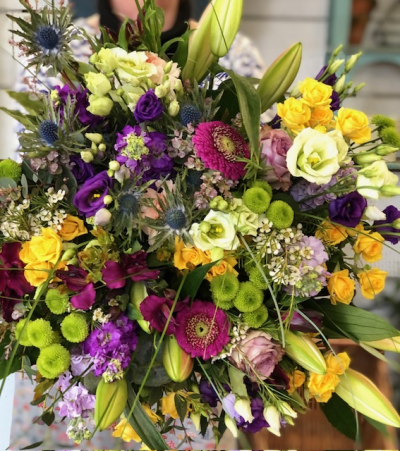 Fields of Cheer - Inspired by the wildflower colour palette of a summer meadow and the warmth of a golden hour, this design is a glorious tangle of bright country blooms in shades of yellow, purple, cerise with pops of bright green and blue. Looking like an armful of nature, freshly picked, this bouquet will turn heads  and lift hearts.