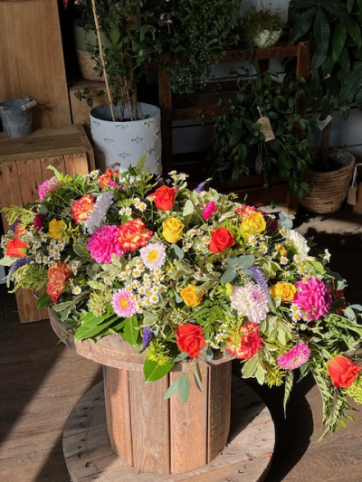 Casket Spray bright - A lively and uplifting casket spray bursting with bold cheerful hues of orange, yellow, cerise and touches of white and purple, set off by the abundant greenery, framing the colour