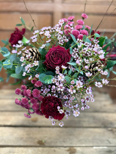 Mulled Berry Magic - A rich, seasonal blend of deep berry tones and soft blush accents, this bouquet brings a cosy winter elegance to any space. Layers of velvety raspberry hues sit beautifully among clusters of delicate pastel blooms, creating a textured, gathered-from-the-woodland feel. Natural greenery adds freshness and movement, while rustic cones and twig-like elements give a subtle nod to the forest in winter. The result is a stylish, modern Christmas arrangement that feels both luxurious and wonderfully natural—perfect for gifting or adding a touch of festive warmth to the home.