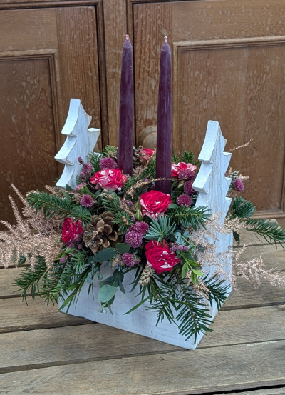 Mulberry Pines arrangement - Bring the magic of a woodland Christmas into your home with this handcrafted festive arrangement. Two deep mulberry taper candles rise from a lush bed of seasonal evergreens, pinecones, and rich berry-toned blooms. Soft touches of gold-tinted foliage add a gentle sparkle, while rustic wooden Christmas trees frame the design for a charming, country-inspired finish.

Perfect for Christmas tables, mantlepieces, or as a welcoming centrepiece for holiday gatherings, this arrangement blends natural textures with warm winter colours—capturing the cosy spirit of the season.