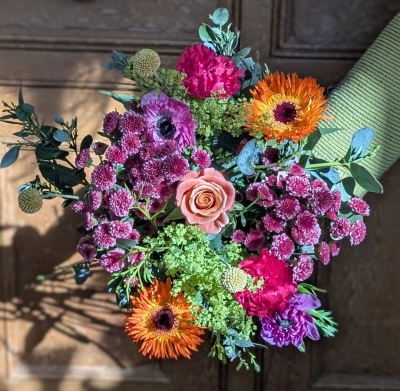 Love in full bloom - This breathtaking arrangement is a symphony of color and devotion, designed to mirror the vibrant warmth of a mother’s heart. At its center rests a single, porcelain-soft bloom in a delicate apricot hue, its petals unfurling in a perfect, eternal spiral—a symbol of the quiet grace at the core of every home.

Surrounding this tender center is a passionate dance of jewel tones. Deep, velvety fuchsia ruffles and mysterious violet petals create a rich tapestry of affection, while brilliant, sun-kissed starbursts of orange radiate outward like a warm embrace. Clusters of tiny, wine-colored globes add a rhythmic, playful charm, nestled among frothy, lace-like greenery that feels as light and airy as a shared laugh.

Finished with silvery, sea-mist foliage and whimsical botanical spheres, this bouquet is more than a gift; it is a lush, living poem. It captures the wild beauty of a summer garden and the refined elegance of a heartfelt "thank you," making it a timeless tribute to the woman who makes life beautiful.