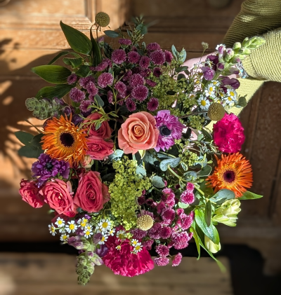 Mother's radiant garden - Mother’s Radiant Garden is a vibrant celebration of warmth, devotion, and everyday heroism. Bursting with sunset oranges, joyful pinks, rich magentas, and soft blush tones, this hand-tied arrangement feels like a walk through a flourishing spring garden at golden hour.

Bold, sun-kissed focal blooms are nestled among clusters of delicate textures and airy accents, while fresh greenery adds depth and a naturally gathered charm. The balance of bright energy and soft romance makes this bouquet both uplifting and heartfelt.

Designed to honour the woman who nurtures, supports, and shines in every season, this arrangement is a colourful reminder that her love is the brightest light of all.