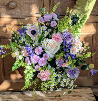 Mother's country meadow - Mother’s Country Meadow captures the gentle beauty of a spring morning in the countryside. Soft ivory and blush tones blend effortlessly with hints of lilac, lavender, and fresh green, creating a bouquet that feels natural, graceful, and full of heartfelt charm.

Delicate, dainty accents weave through romantic, ruffled petals and elegant focal blooms, while textured greenery adds a just-gathered-from-the-garden feel. Airy sprigs and trailing details give the arrangement movement and softness, like wild blossoms dancing in a light breeze.

Perfect for the mum who loves timeless elegance with a rustic twist, this bouquet is a tender expression of gratitude, comfort, and unconditional love — as wholesome and beautiful as she is.